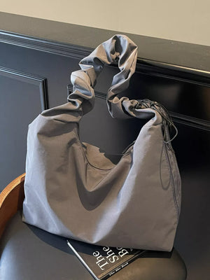 Gray ruched nylon shoulder bag with zipper and decorative tassels.