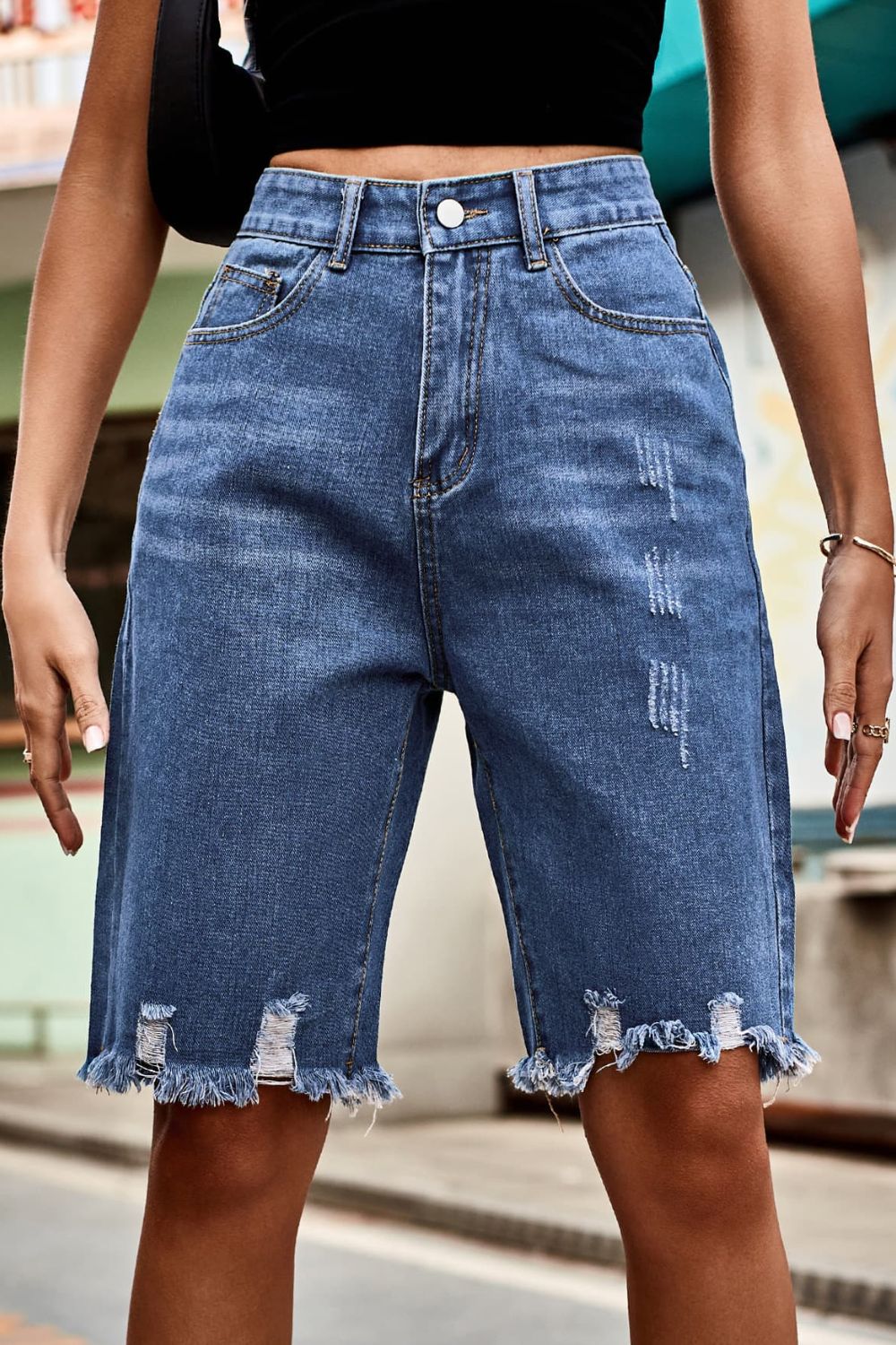 Medium wash denim bermuda shorts with frayed hem and distressed details.