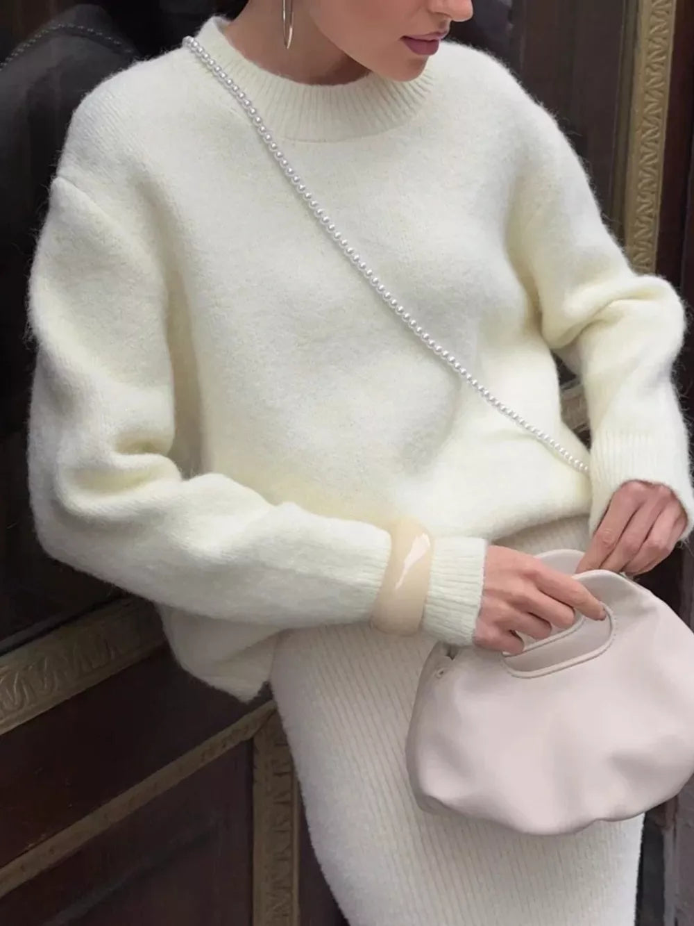 Cozy knit top in cream with relaxed fit and crew neck, styled with a pearl bag.