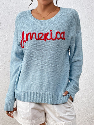 Pastel blue knit sweater with red embroidered "America" text, crew neck, long sleeves.