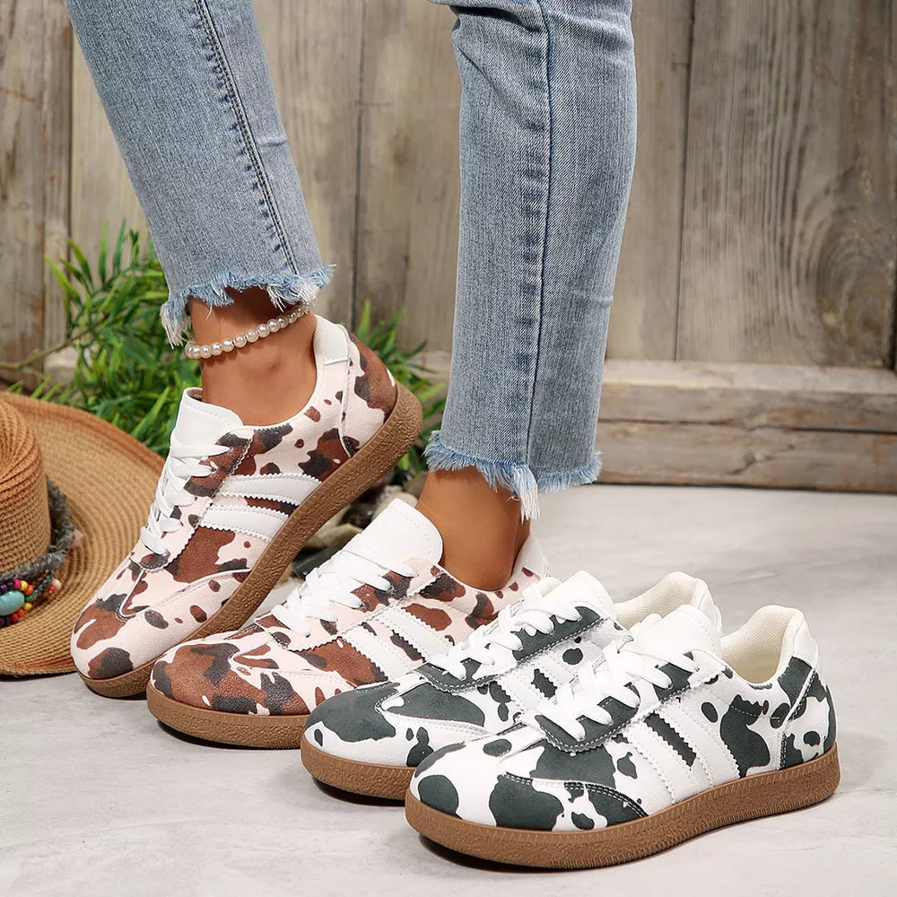 Trendy cow print low-top sneakers in brown and black with white stripes and gum soles.