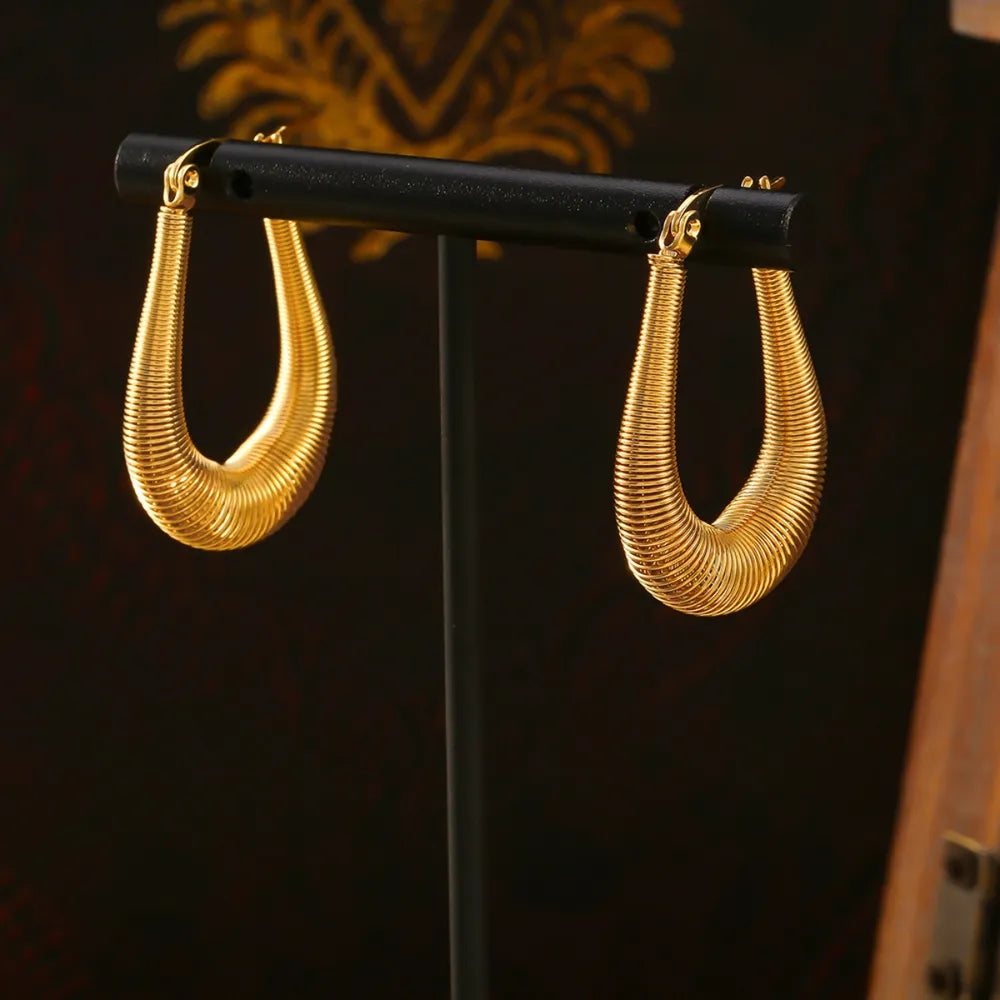 Gold oval hoop earrings with a coiled texture, displayed on a stand.