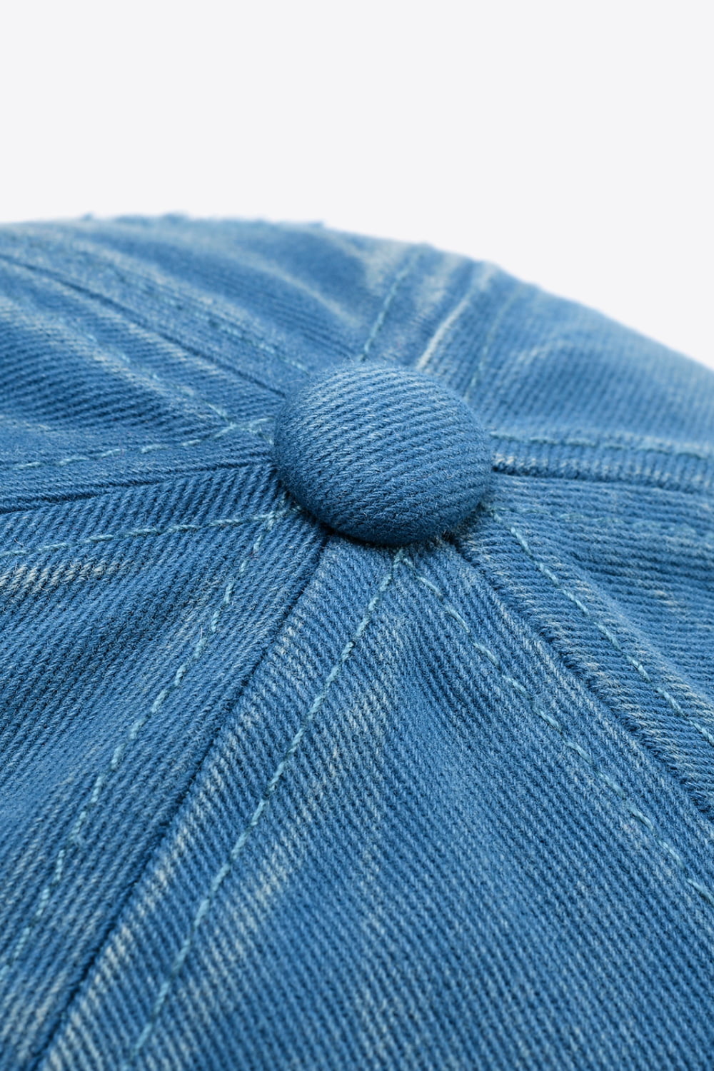 Baseball cap in blue denim with visible stitching and a button detail.