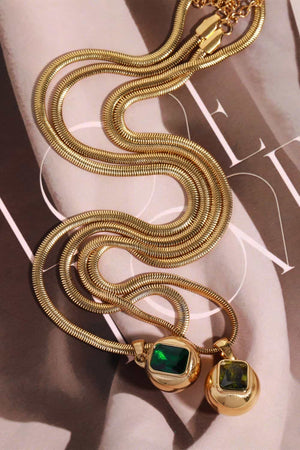 Gold snake chain necklace with two pendants: one orb with a green square stone, one orb with a dark green square stone.