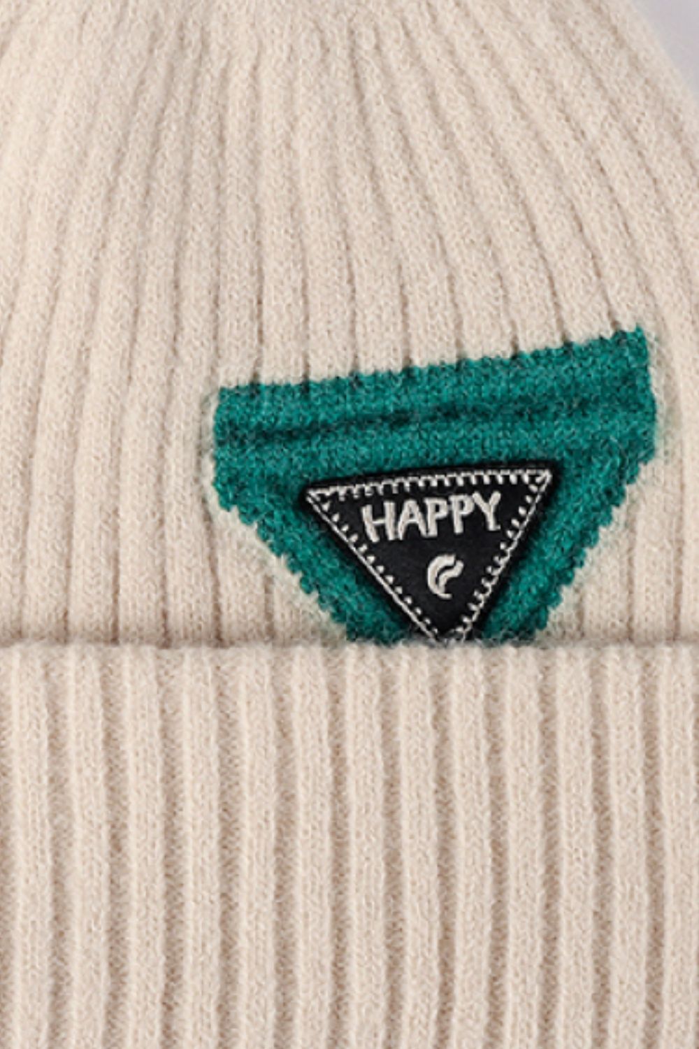 Beige ribbed acrylic beanie with a green patch and "HAPPY" detail.