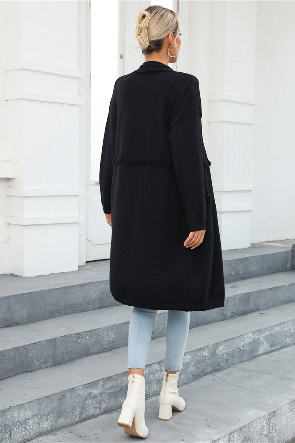 Black longline knit cardigan with fringe trim detail and pockets, worn open.