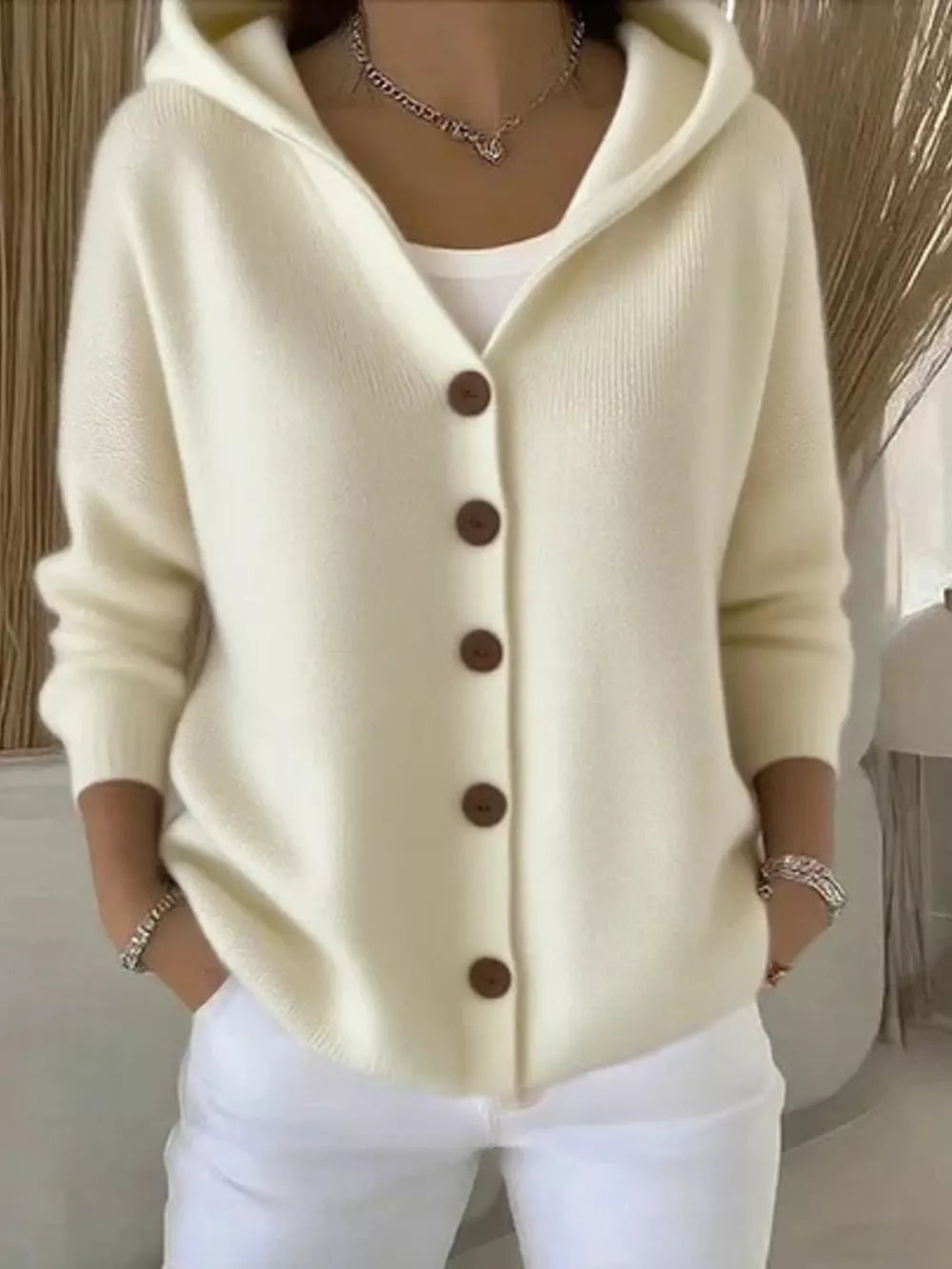 Cream hooded button-front knit cardigan with brown buttons, styled with a white tank and white pants.