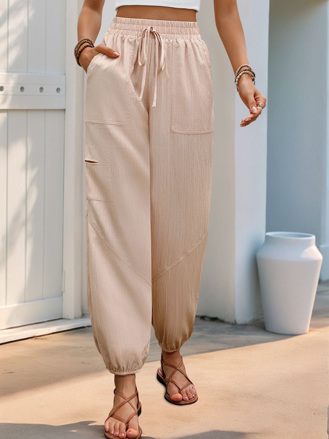 Textured tan cargo pants with drawstring waist and elastic cuffs, featuring multiple pockets.