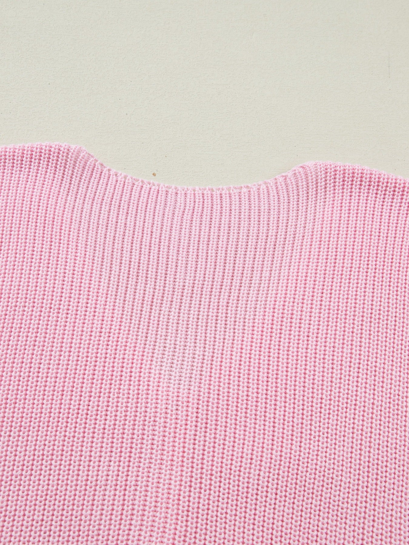 Pink acrylic sweater vest with V-neck detail and ribbed knit texture.