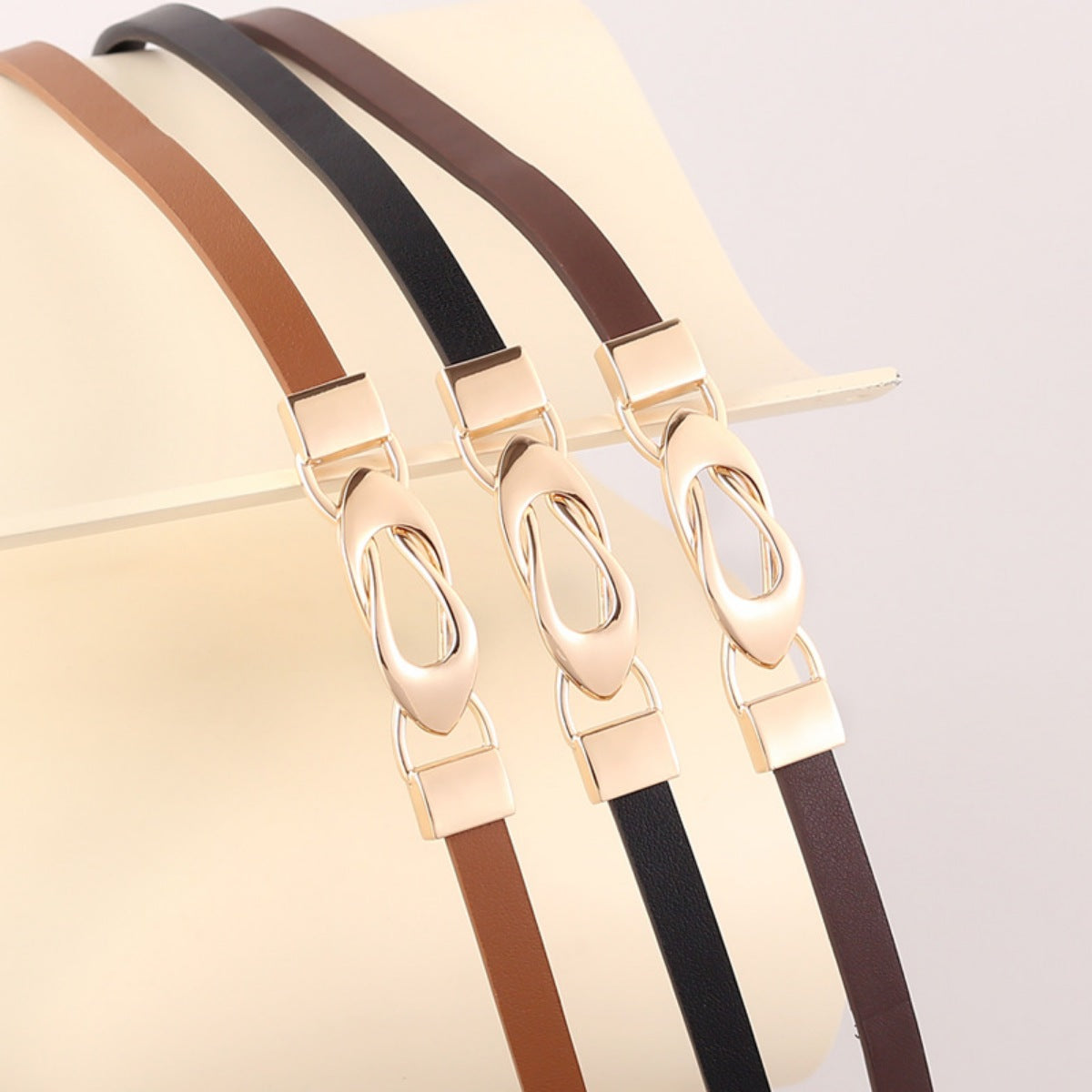 Elegant leather belts in brown, black, and caramel with interlocking gold buckles.