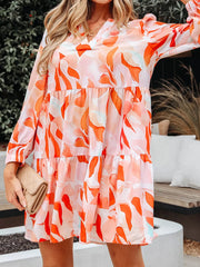 Tiered mini dress with abstract print, V-neck, long sleeves, and flowy skirt.
