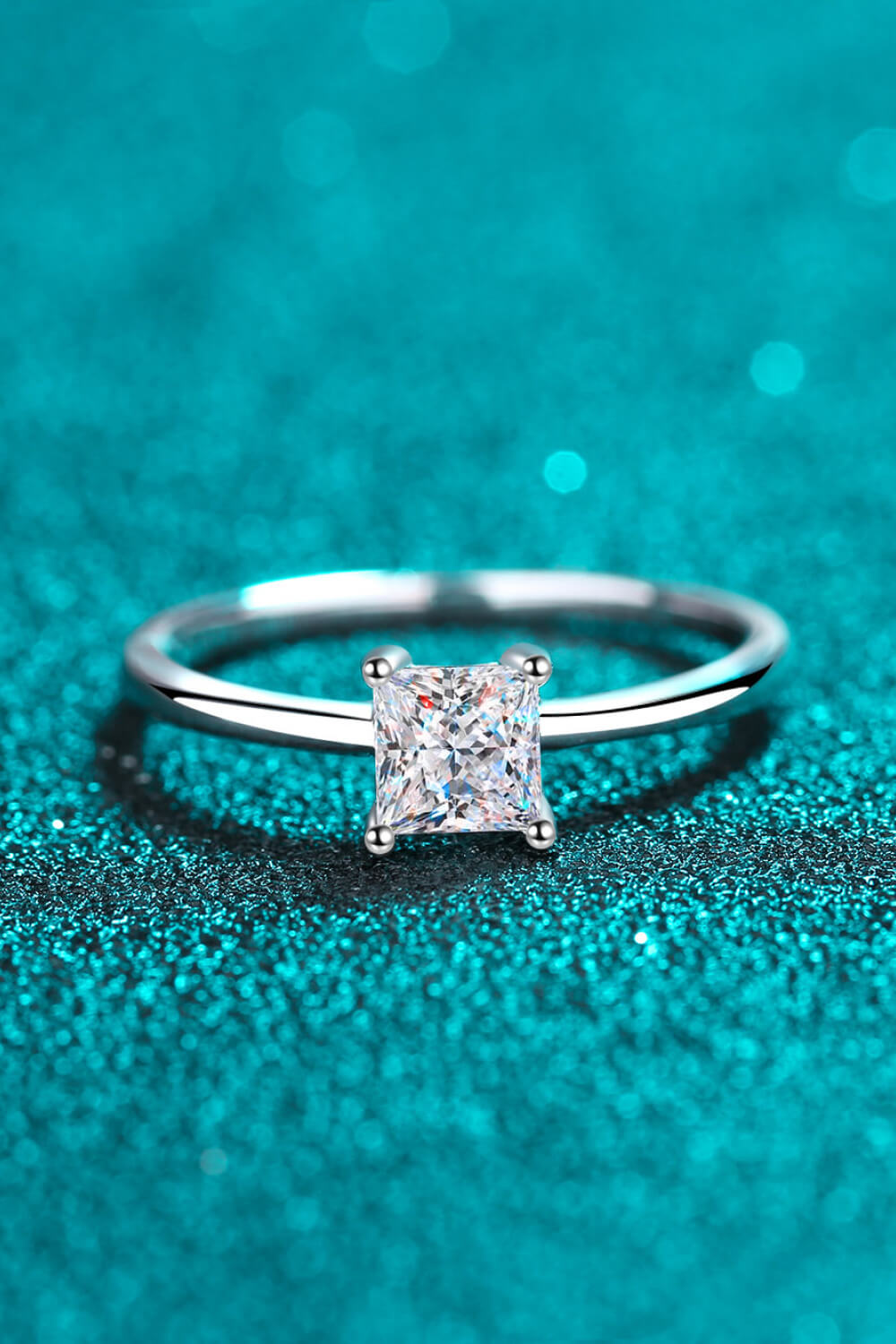 Silver ring with a square cut moissanite diamond on a sparkly blue background.