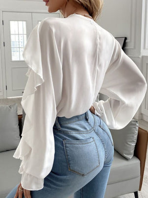 White blouse with ruffled sleeves and V-neck, paired with light wash denim jeans.