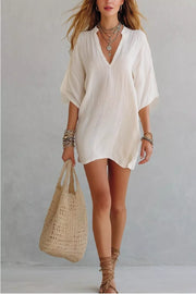 Relaxed white linen-blend mini dress with V-neck and half sleeves, styled with layered necklaces.