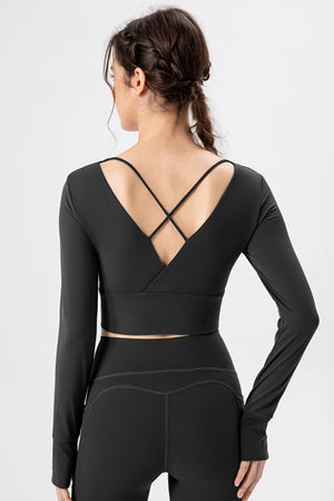 Black crop top with V-neck, criss-cross back straps, long sleeves with thumbholes.