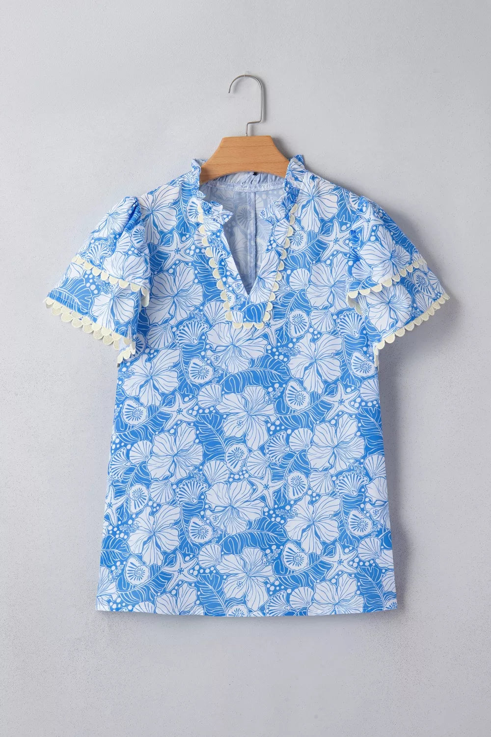 Blue tropical floral print v-neck blouse with frill trim and short sleeves.