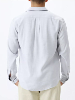 Relaxed camp collar button-up shirt in light blue with back pleats and buttoned cuffs.
