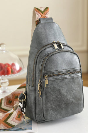 Gray sling bag with geometric strap and multiple zippered pockets.