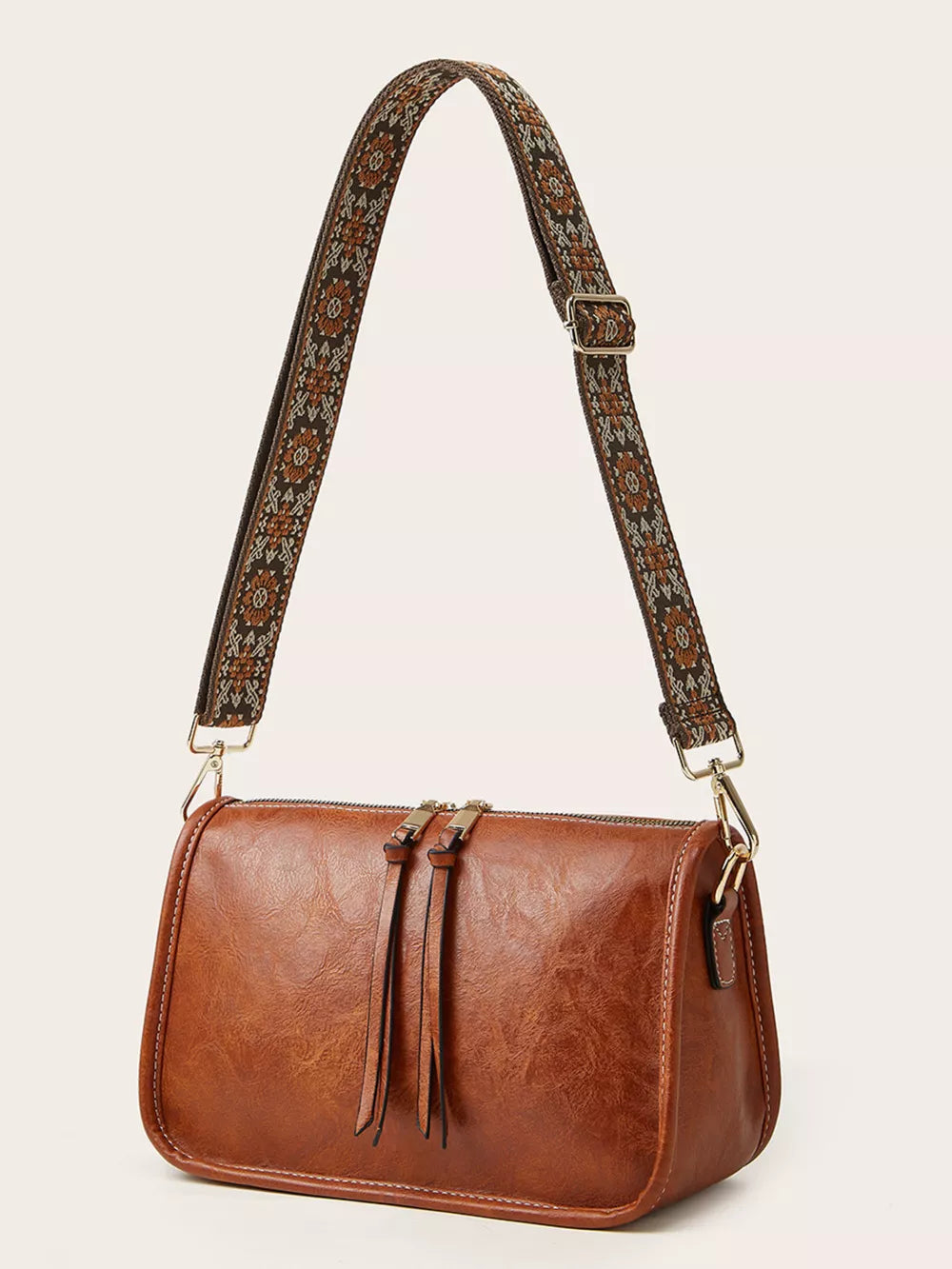 Tan leather crossbody bag with a patterned strap and tassel zipper pulls.
