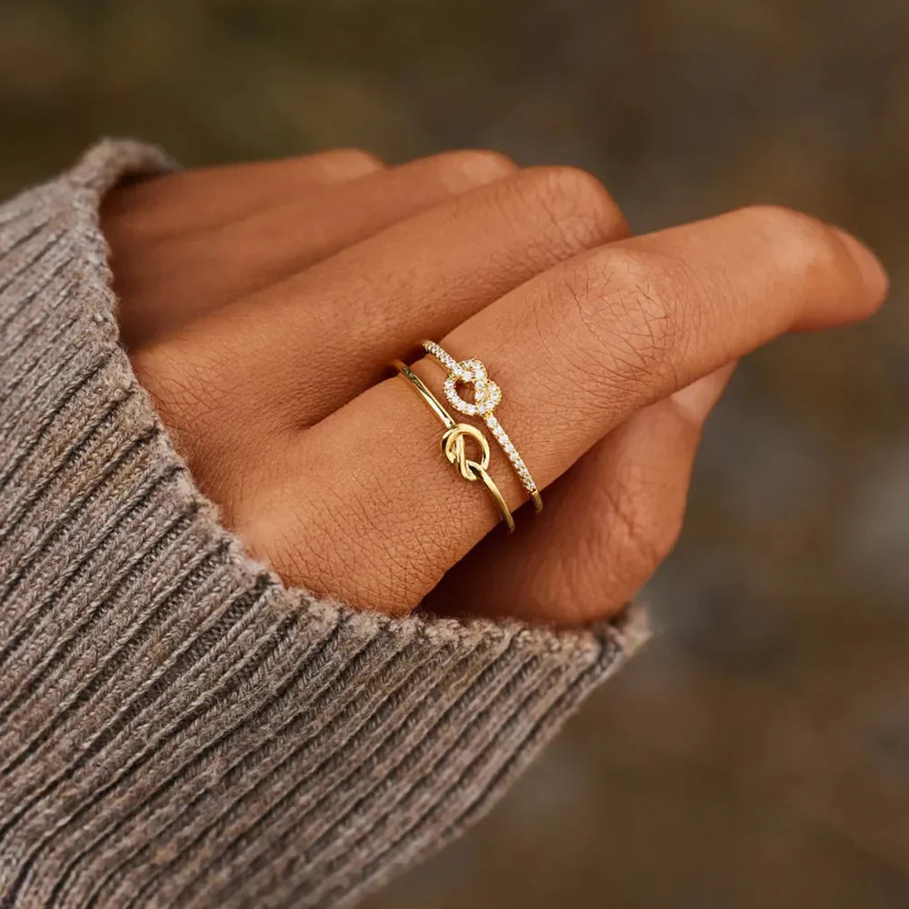 Gold knot ring set with pavé details on a hand wearing a grey sweater.