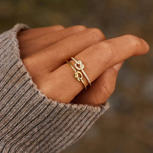 Gold knot ring set with pavé details on a hand wearing a grey sweater.