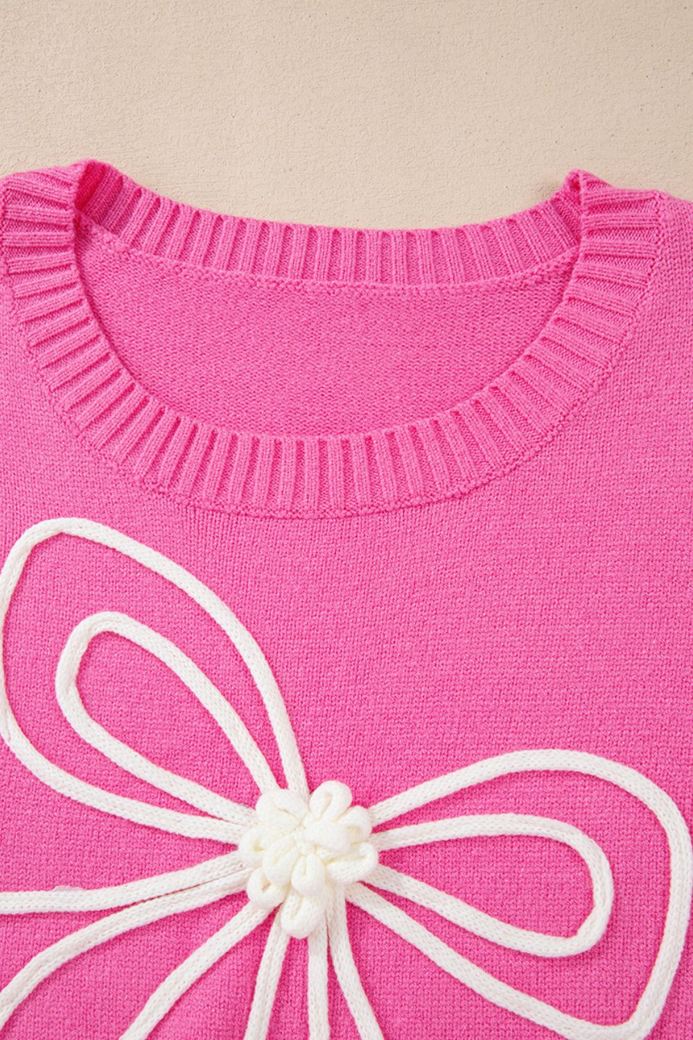 Fuchsia pink knit sweater with a white embroidered bow motif and ribbed crewneck.