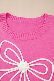 Fuchsia pink knit sweater with a white embroidered bow motif and ribbed crewneck.