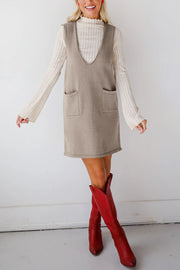 Sleeveless knit dress in gray with V-neck and two front pockets, shown over a cream ribbed turtleneck.