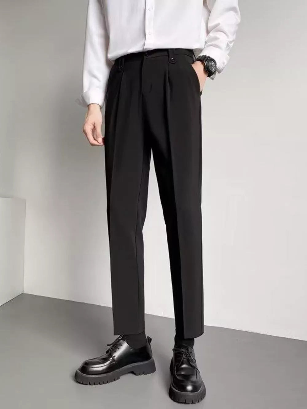 Black ankle length trousers with pleats and a slim fit, styled with a white shirt and black shoes.