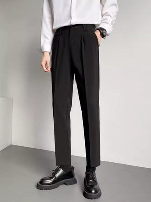 Black ankle length trousers with pleats and a slim fit, styled with a white shirt and black shoes.