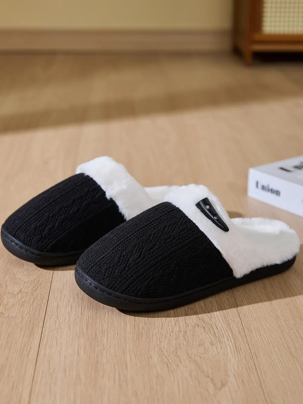 Black cable knit shearling house slippers with white faux fur lining and decorative button detail.