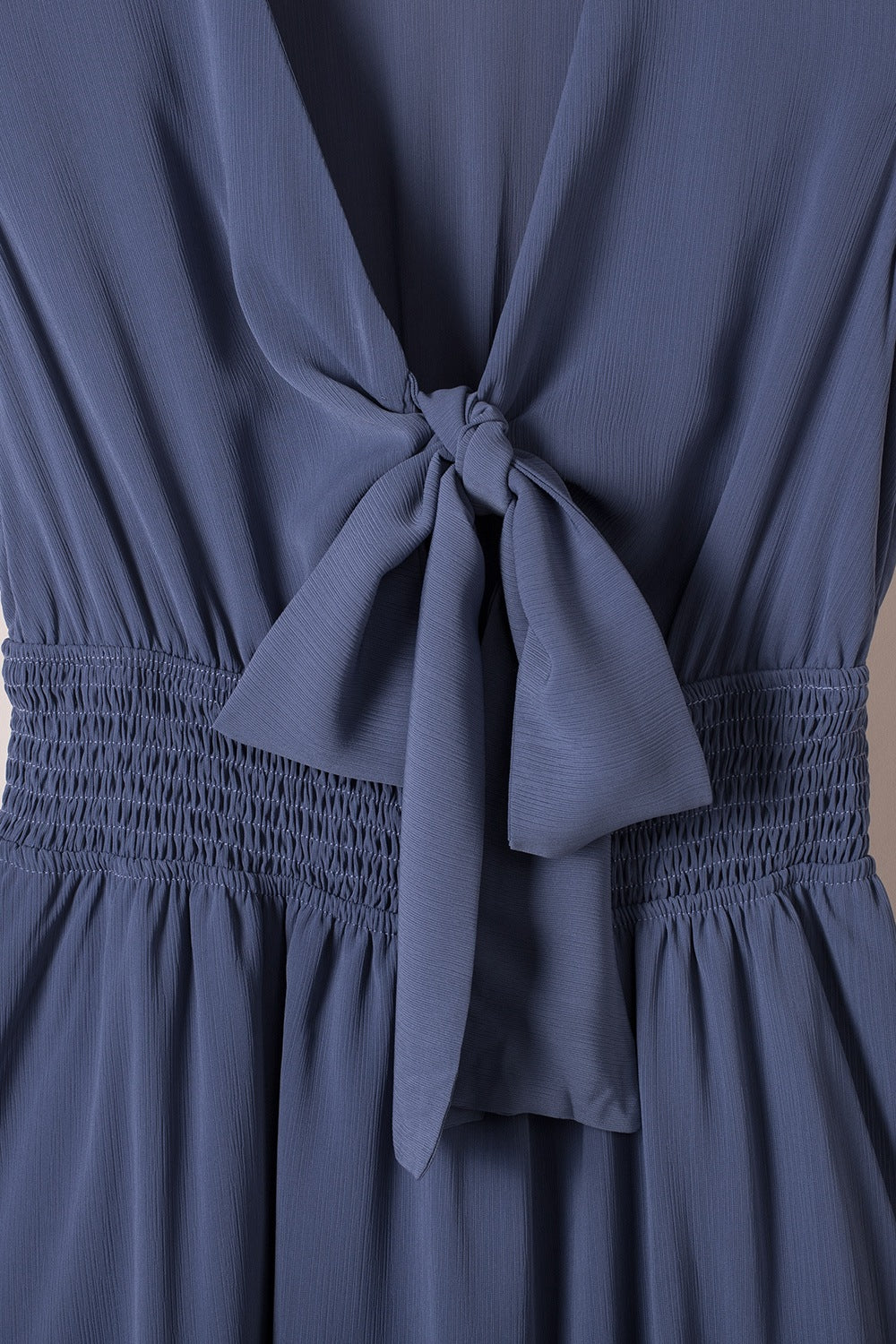 Dusty blue mini dress with V-neck, ruffled bow tie, and smocked waist.