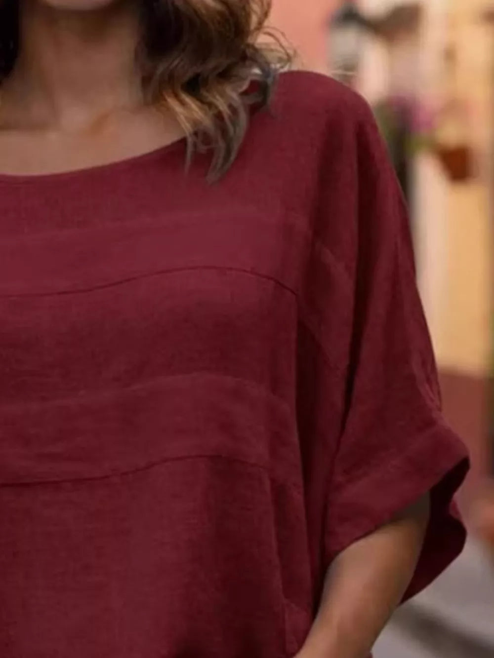 Wine red relaxed fit blouse with short sleeves and curved seam details.