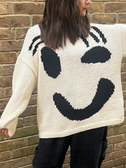 Cream knit sweater with a playful black abstract smiley face graphic and long sleeves.
