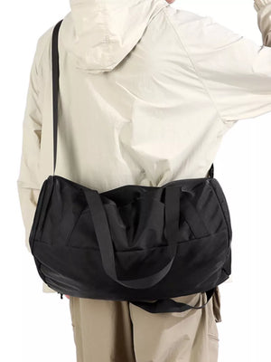 Black barrel duffel bag with zippered pocket and shoulder strap, worn crossbody.