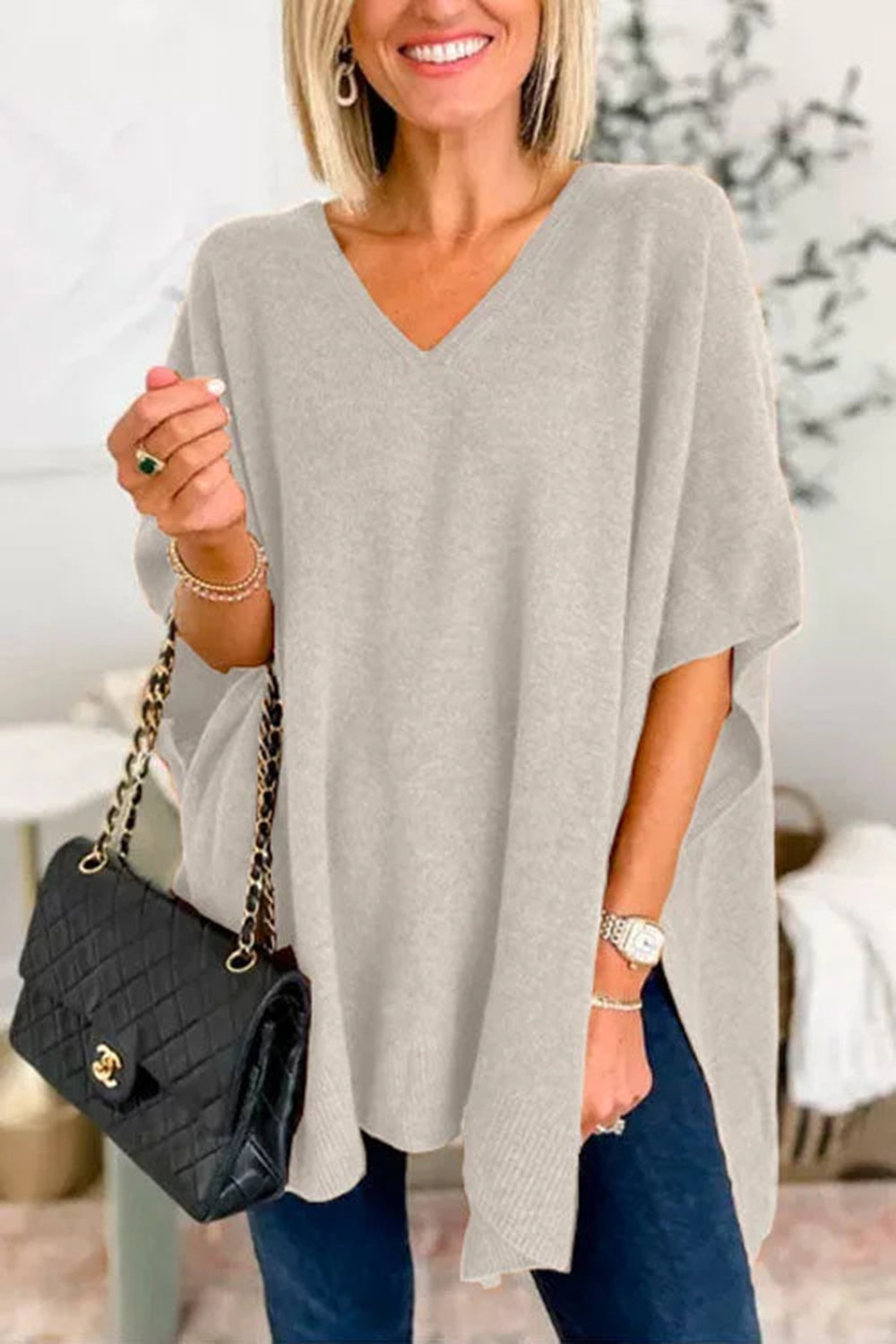 Light Gray V-neck knit poncho top with relaxed fit and side slits, styled with a black quilted handbag.
