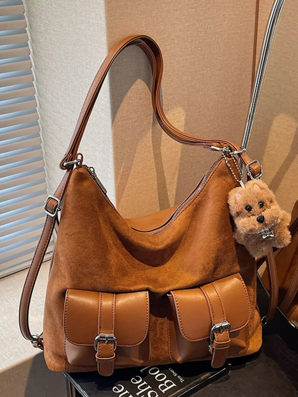 Brown suede half-moon handbag with two front buckle pockets and a fluffy dog charm.