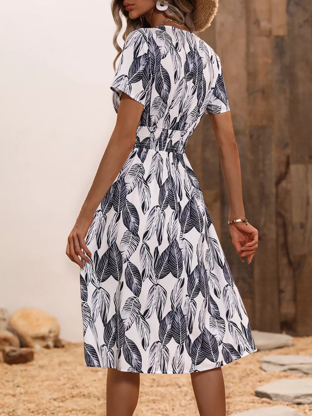 A-line midi dress in white with a black leaf pattern, v-neck, short sleeves, and cinched waist.