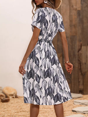 A-line midi dress in white with a black leaf pattern, v-neck, short sleeves, and cinched waist.