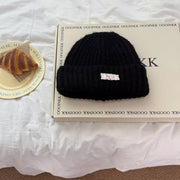 Black chunky knit beanie with a white decorative label.