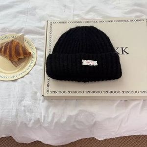 Black chunky knit beanie with a white decorative label.