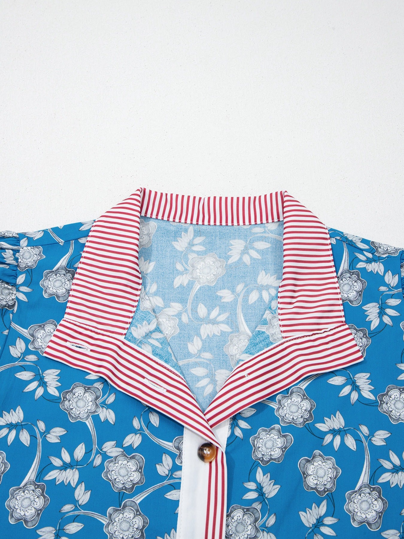 Blue floral cotton blouse with red and white striped collar and button detail.