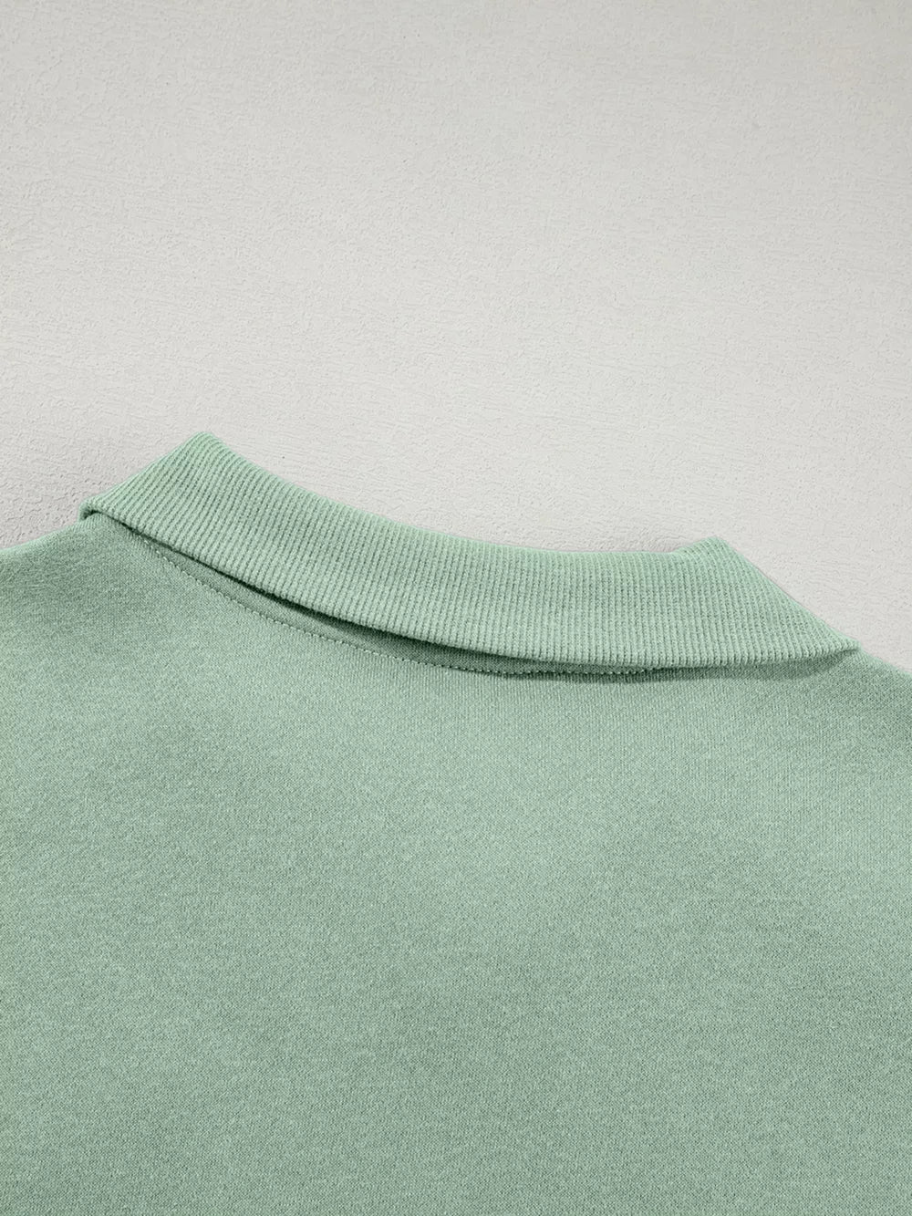 Sage zip-up jacket detail with ribbed collar and cotton fabric.
