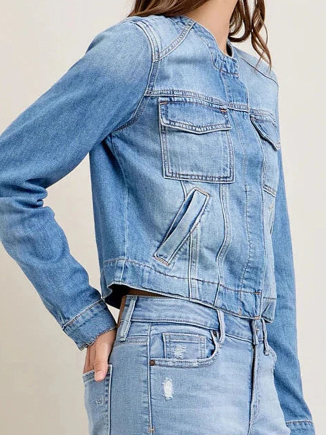 Light wash denim trucker jacket with band collar, chest pockets and side pockets.