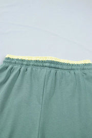 Green cotton sweatpants with yellow drawstring waist and wide legs.