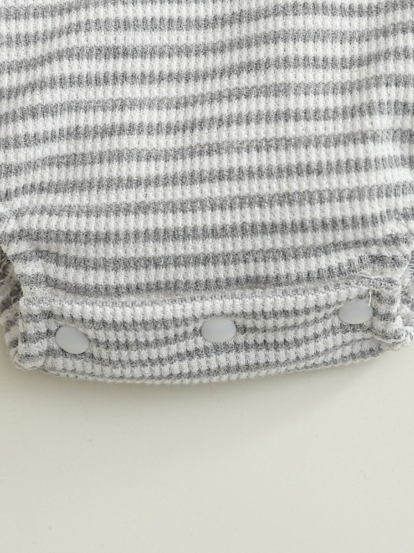Baby one-piece with grey and white stripes, waffle knit, and snap closures.