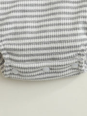 Baby one-piece with grey and white stripes, waffle knit, and snap closures.
