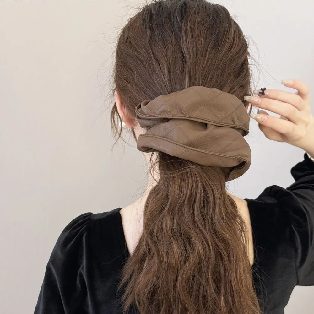 Brown quilted faux leather scrunchie with diamond stitching detail on brown hair.