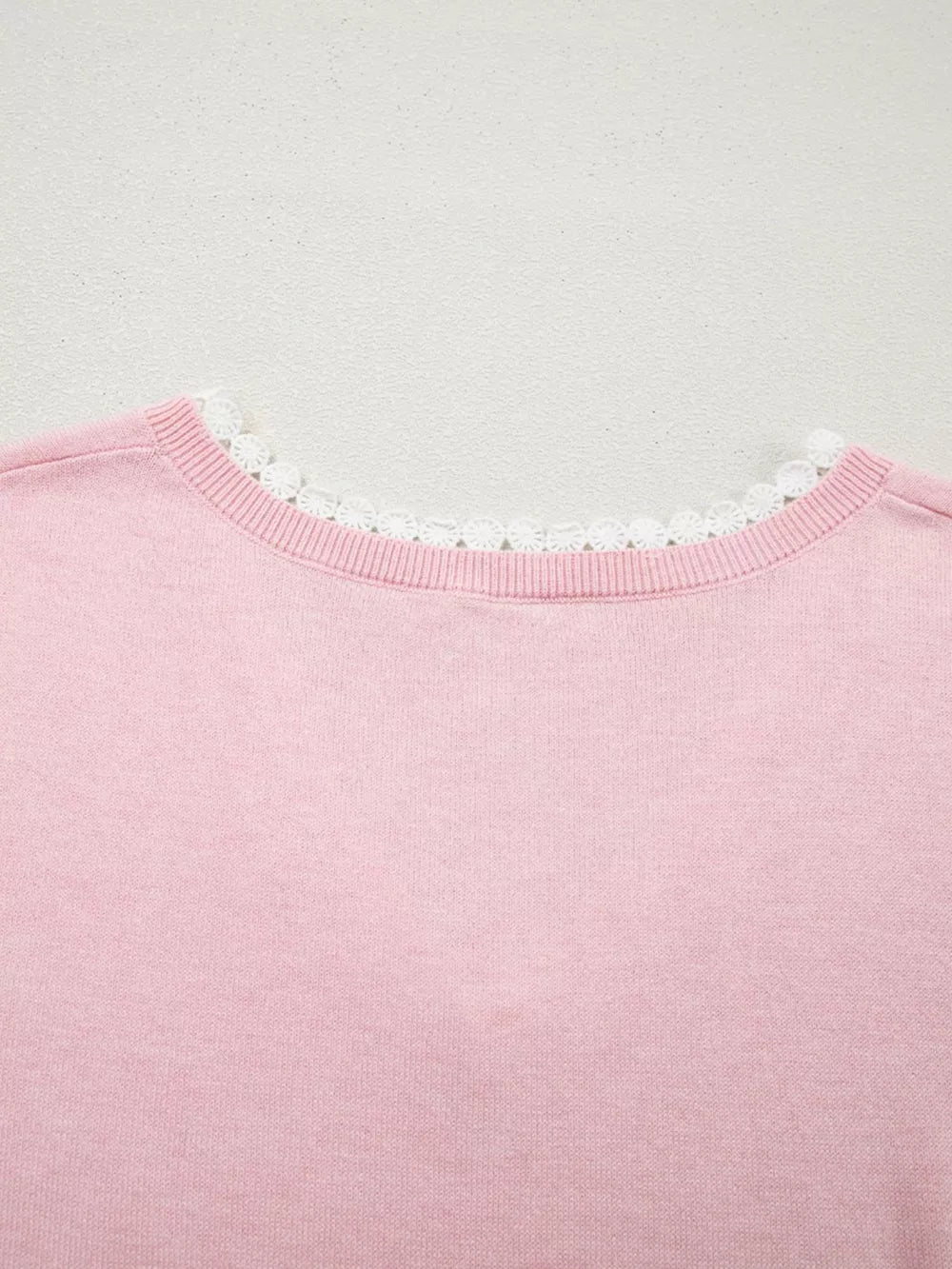 Pink knit top with delicate white lace trim at the V-neckline.