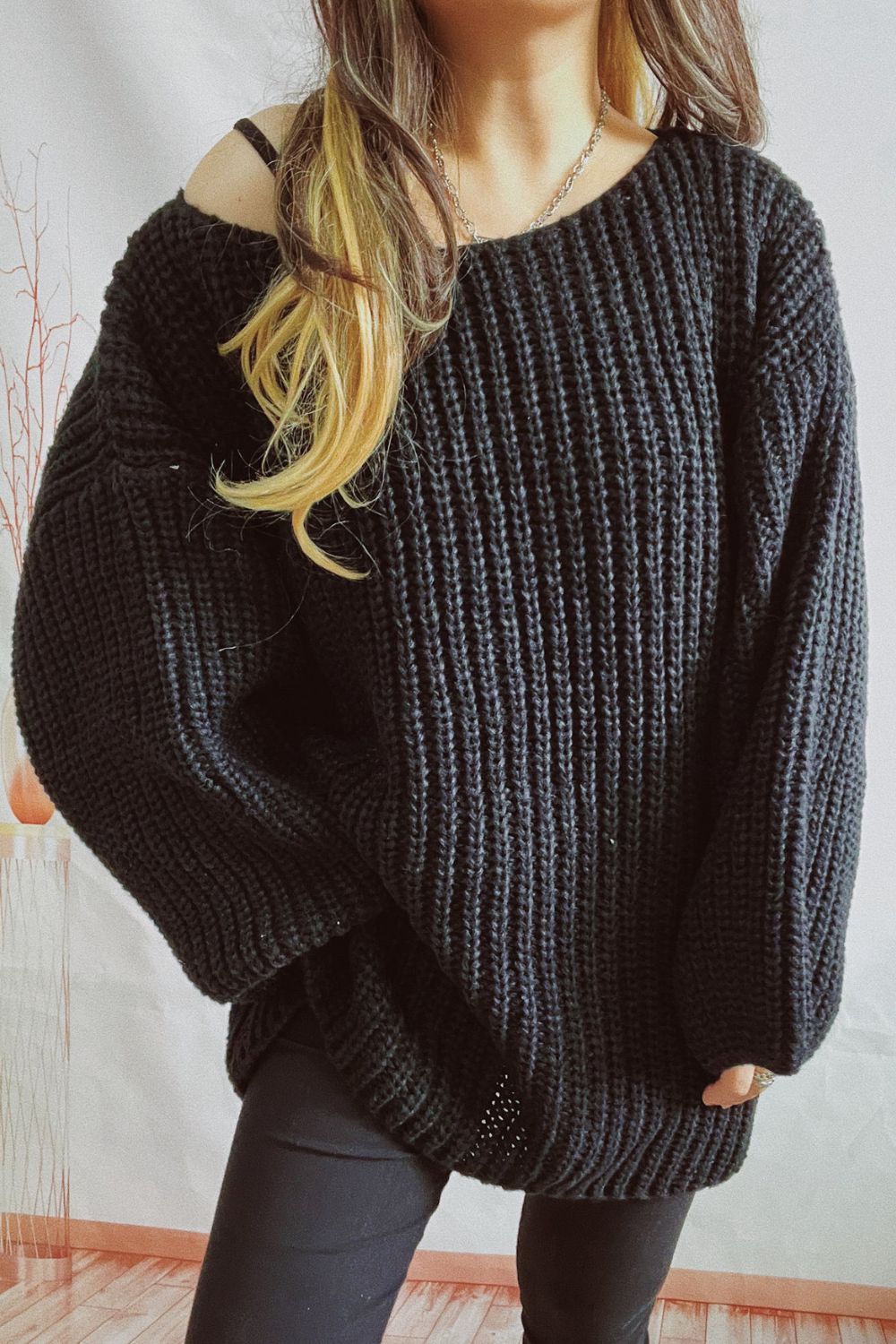 Black oversized ribbed knit sweater with boat neck and off-the-shoulder styling.